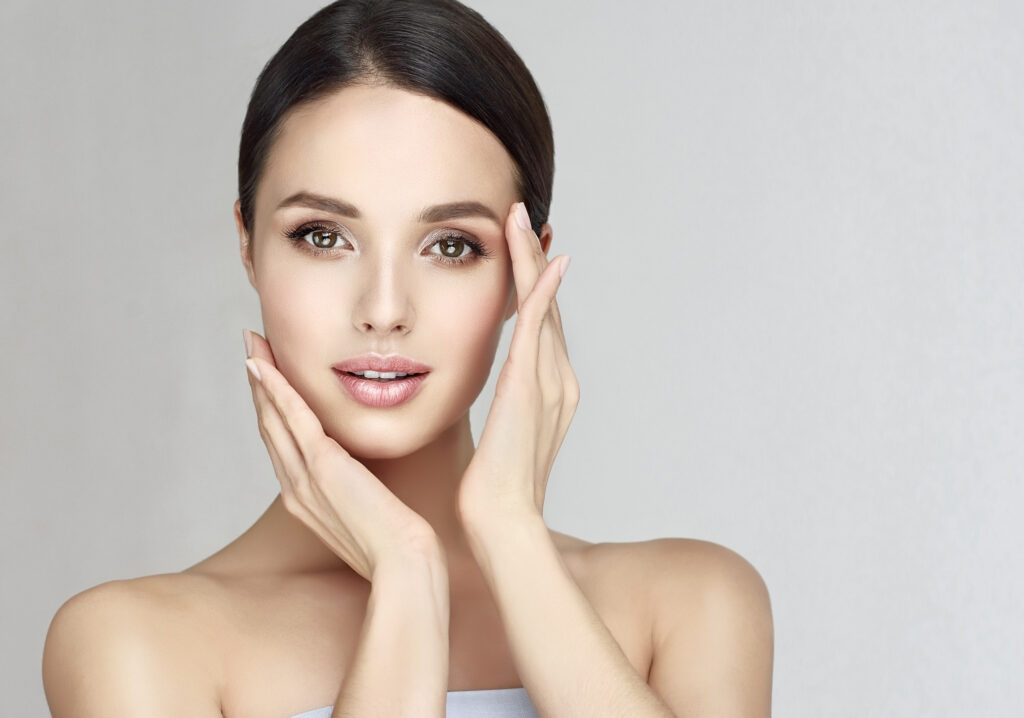 Gorgeous, young woman with clean, fresh skin is touching own face. Light smile on the perfect face. Cosmetology.