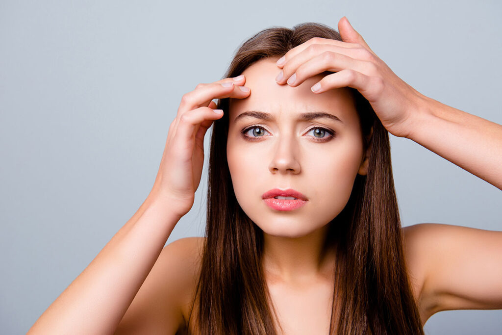 Young woman feeling her forehead looking for all forms of acne breakouts such as inflammatory or noninflammatory acne.